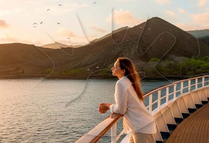 Woman in white shirt and beige pants admiring the sunset from a yacht railing in the Galapagos, with seagulls in the sky